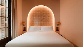 A neatly made bed with a large, illuminated dome-shaped ceiling light fixture above it.