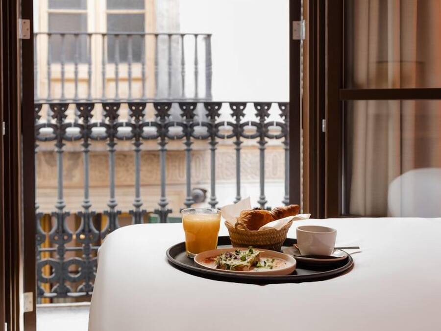 A breakfast tray with toast, a cup, and a glass of orange juice on a bed in a hotel room with a balcony view.