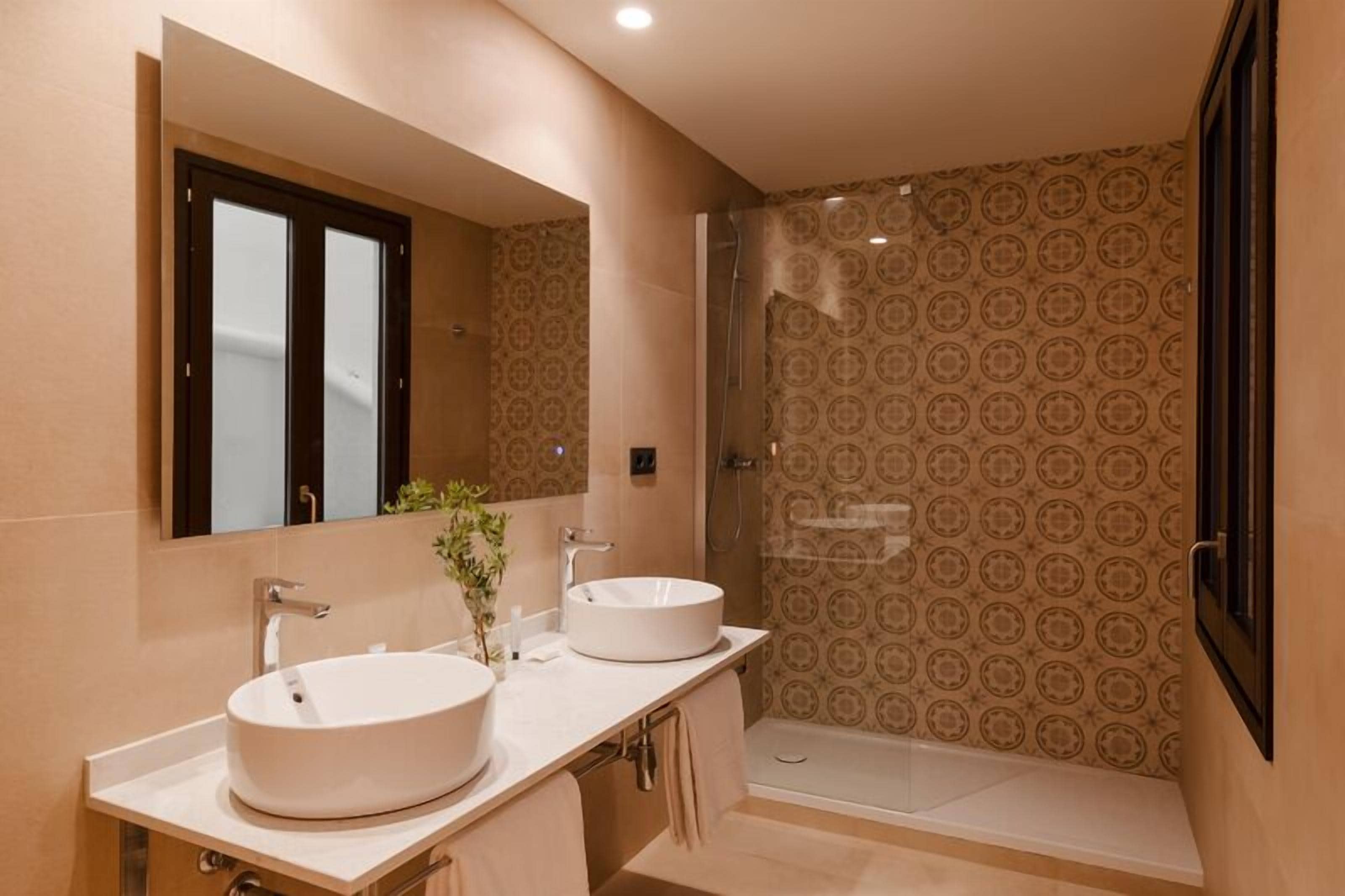 Een badkamer met twee wasbakken, een douche en behang met een patroon.