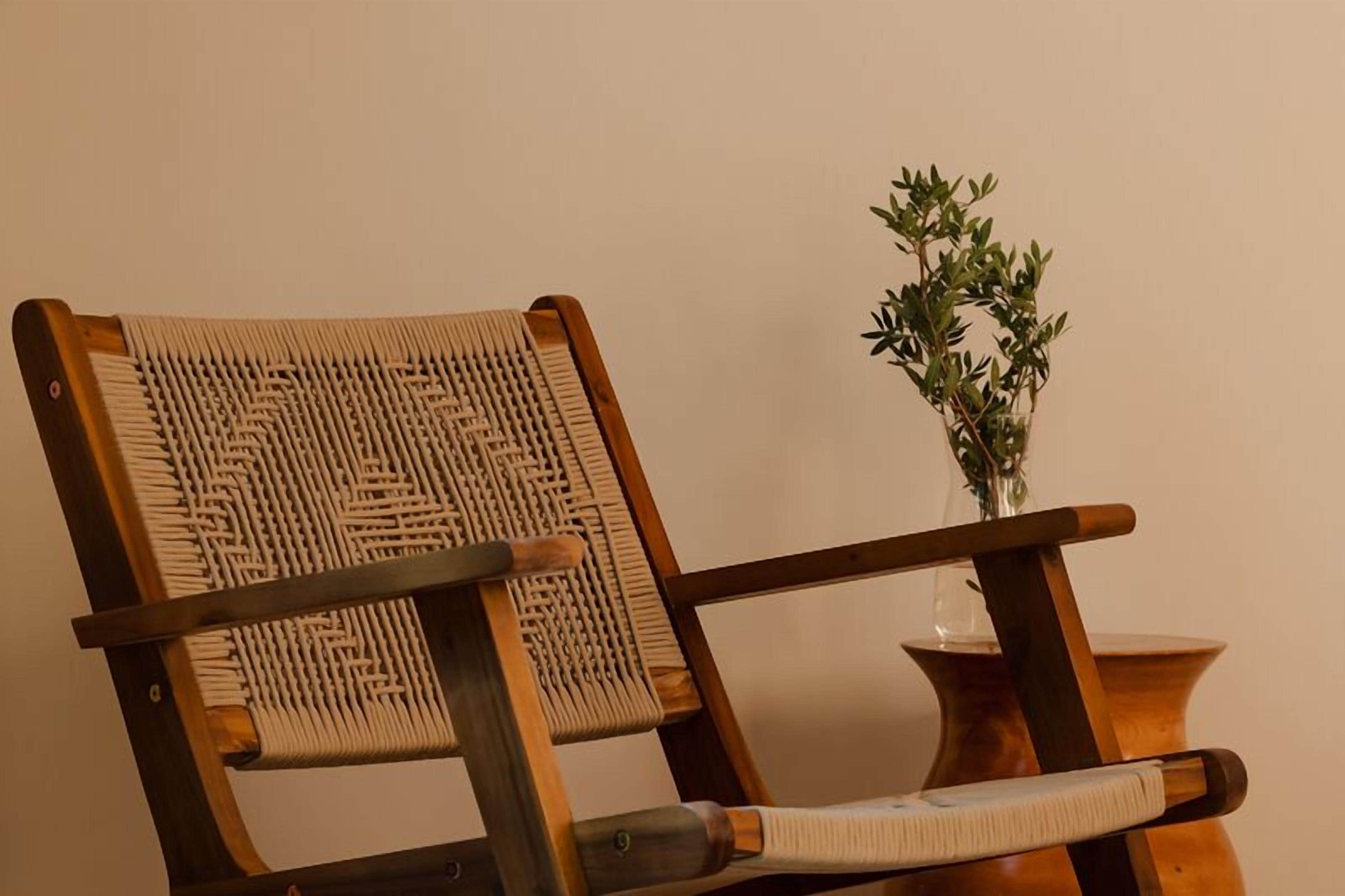 A wooden chair with a woven backrest and seat, placed next to a small wooden table with a vase of green plants.