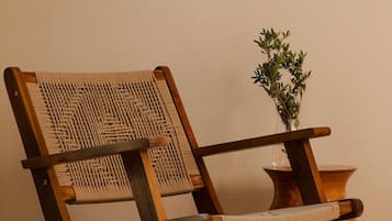 A wooden chair with a woven backrest and seat, placed next to a small wooden table with a vase of green plants.
