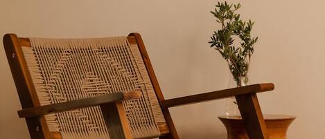 A wooden chair with a woven backrest and seat, placed next to a small wooden table with a vase of green plants.