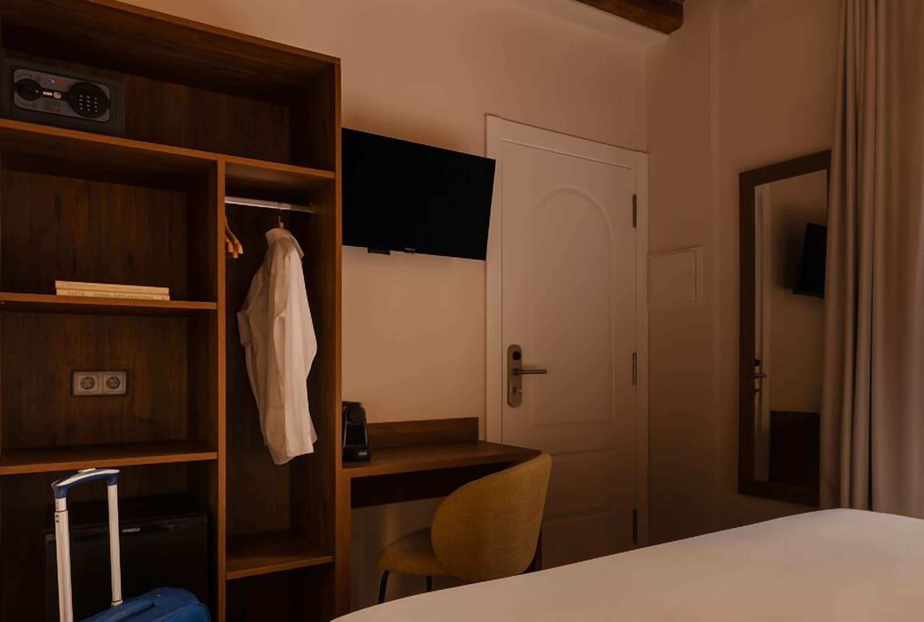 Une chambre d’hôtel équipée d’une armoire en bois, d’un bureau avec une chaise, d’un lit et d’un téléviseur fixé au mur.