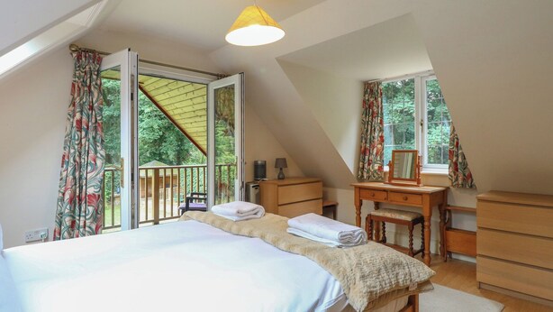 A bedroom with a bed, a dresser, a desk with a mirror, and a window with curtains. - The Anchorage (Norwich)