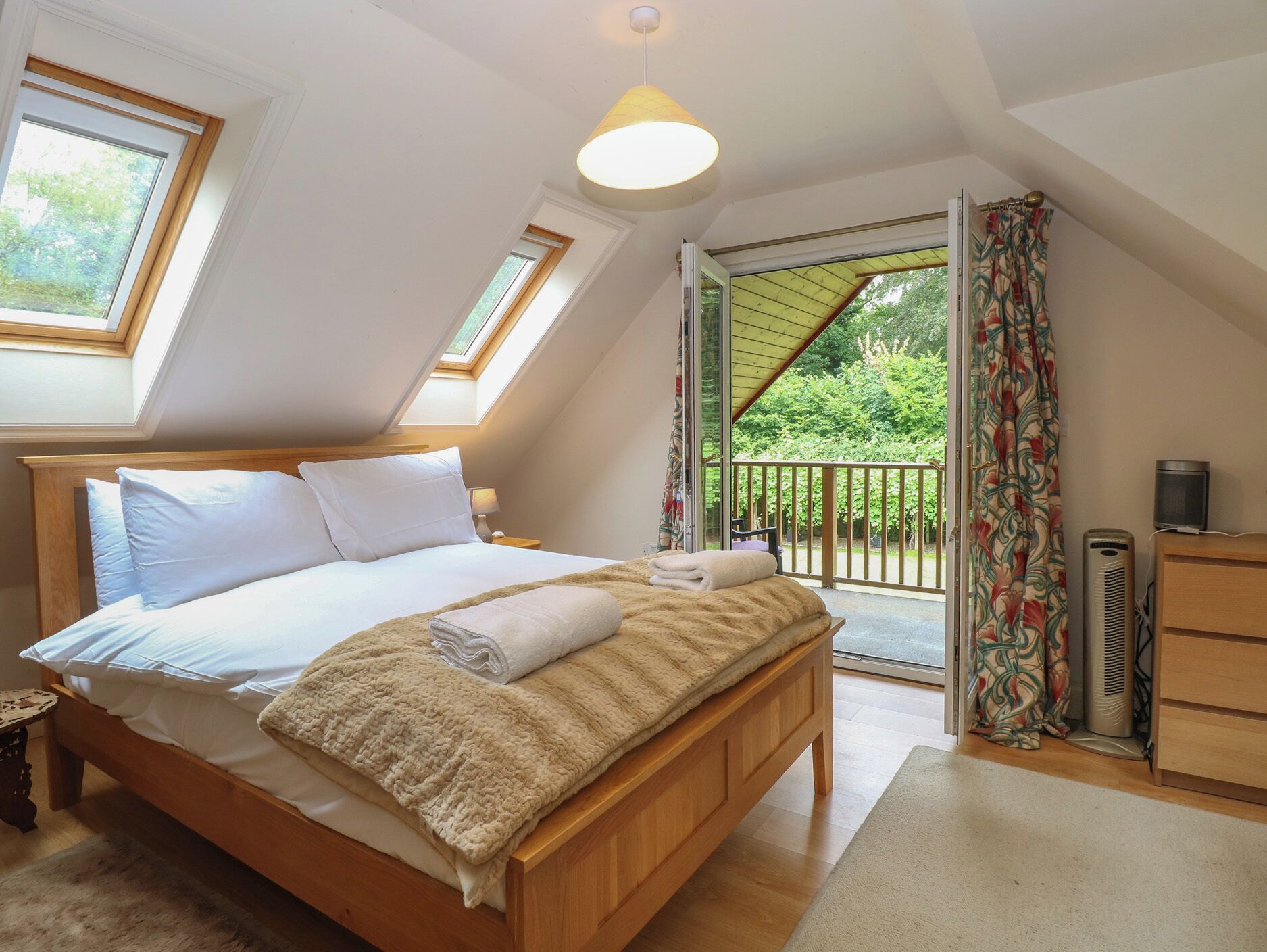 A bedroom with a wooden bed, a skylight, a balcony with a view of greenery, and a heater.