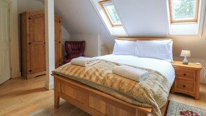 A bedroom with a wooden bed, a nightstand, a lamp, and a window. - The Anchorage (Norwich)