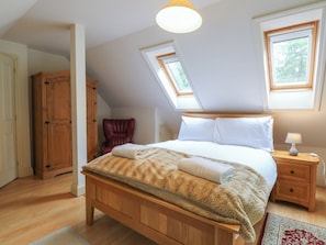 Een slaapkamer met een houten bed, een nachtkastje, een lamp en een raam.