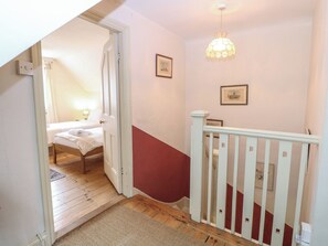 Ein Schlafzimmer mit einem Bett, einem Nachttisch und einer Lampe. Eine Treppe mit Geländer führt zu einer oberen Etage.