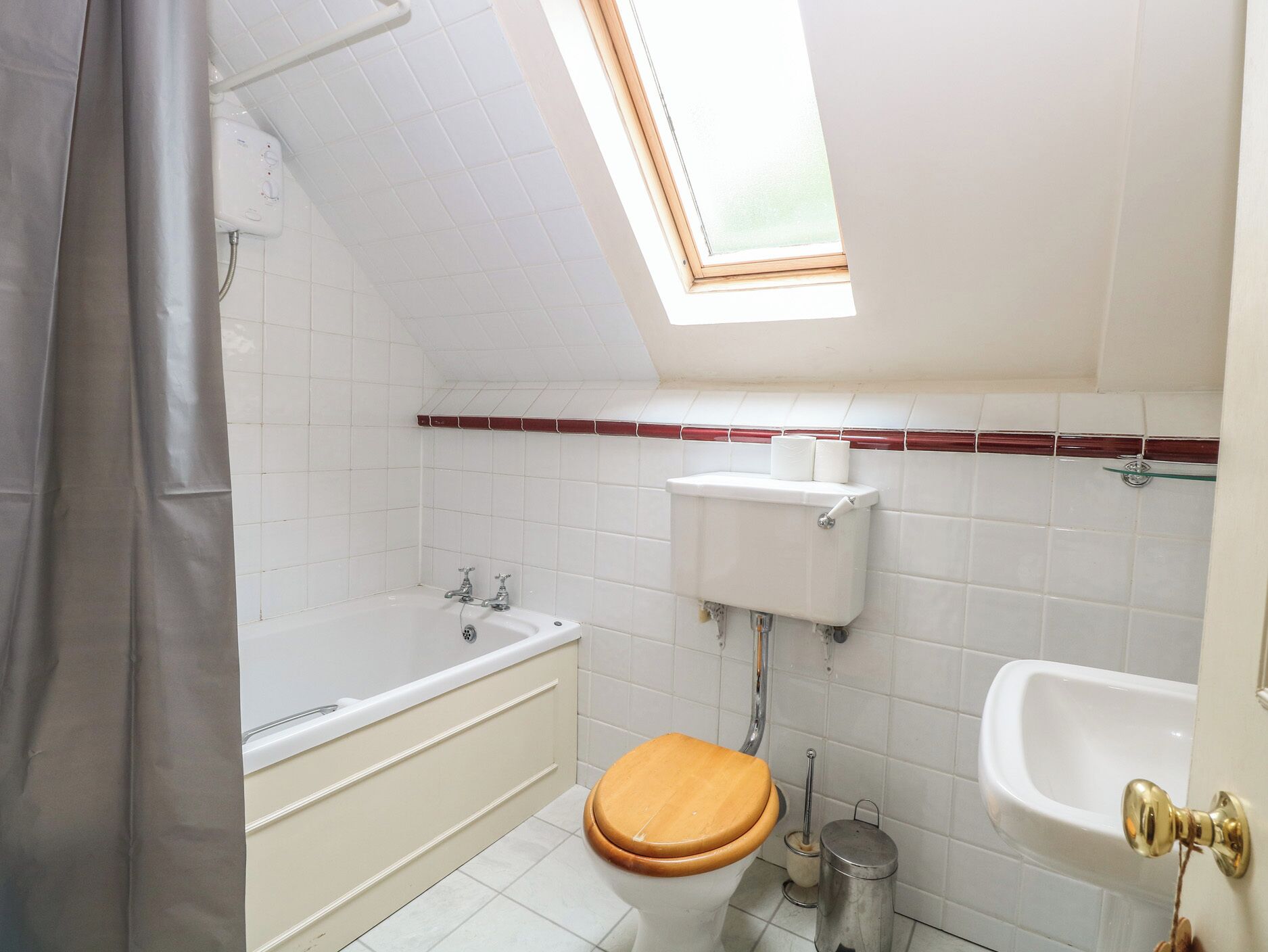 A bathroom with a skylight, a bathtub, a toilet, and a sink.