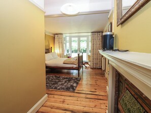 A narrow hallway leading to a bedroom with a bed, a radiator, and a window with curtains. - The Anchorage (Norwich)