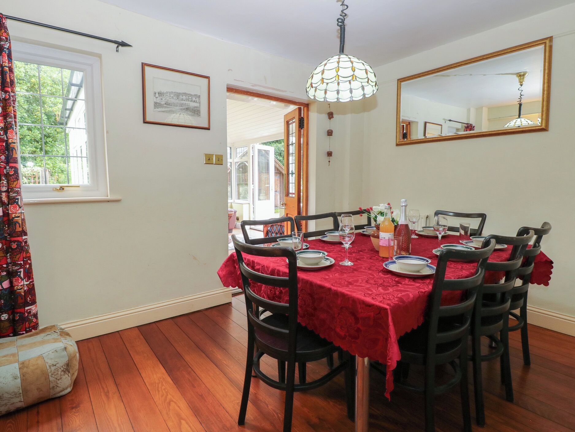 A dining area with a table set for six, surrounded by chairs, a chandelier, and a large mirror on the wall.