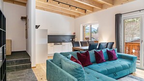 A modern living room with a teal sofa, a staircase, and a kitchen area.