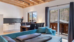 A modern room with a bed, a dining table with chairs, a kitchen area, and large windows with a view of trees.