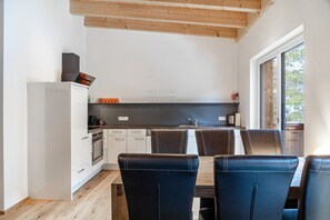 A modern kitchen with white cabinets, a wooden ceiling, and a dining area with dark chairs. - Apartment 'Lorenz' with Mountain View, Balcony and Wi-Fi (Scharnitz)
