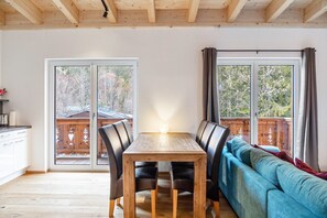 A dining area with a wooden table and chairs, a sofa, and large windows with curtains. - Apartment 'Lorenz' with Mountain View, Balcony and Wi-Fi (Scharnitz)