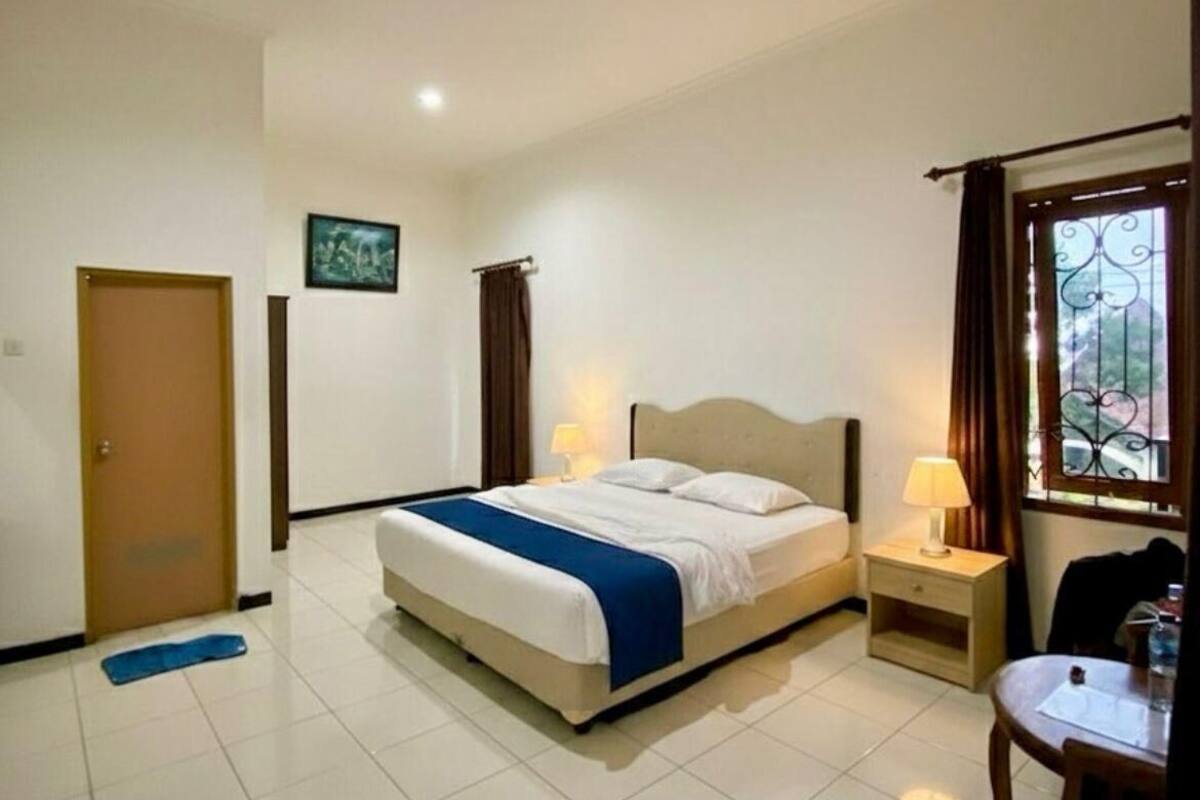 Une chambre d’hôtel avec un lit, des tables de chevet, une chaise et une fenêtre avec des rideaux.
