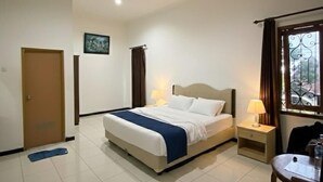 Una habitación de hotel con cama, mesita de noche, silla y una pequeña mesa con otra silla.