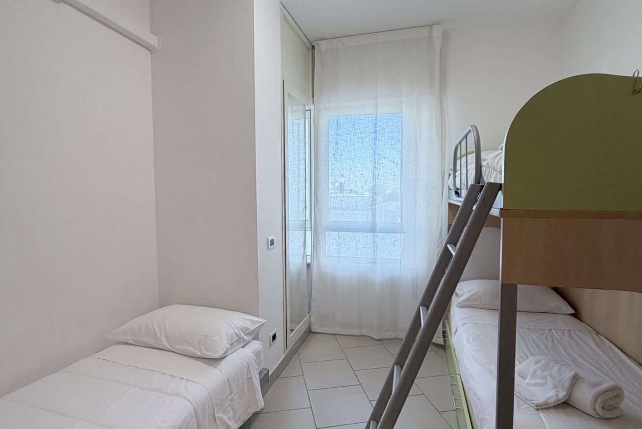 A small, clean room with two single beds, a window with sheer curtains, and a wooden ladder.