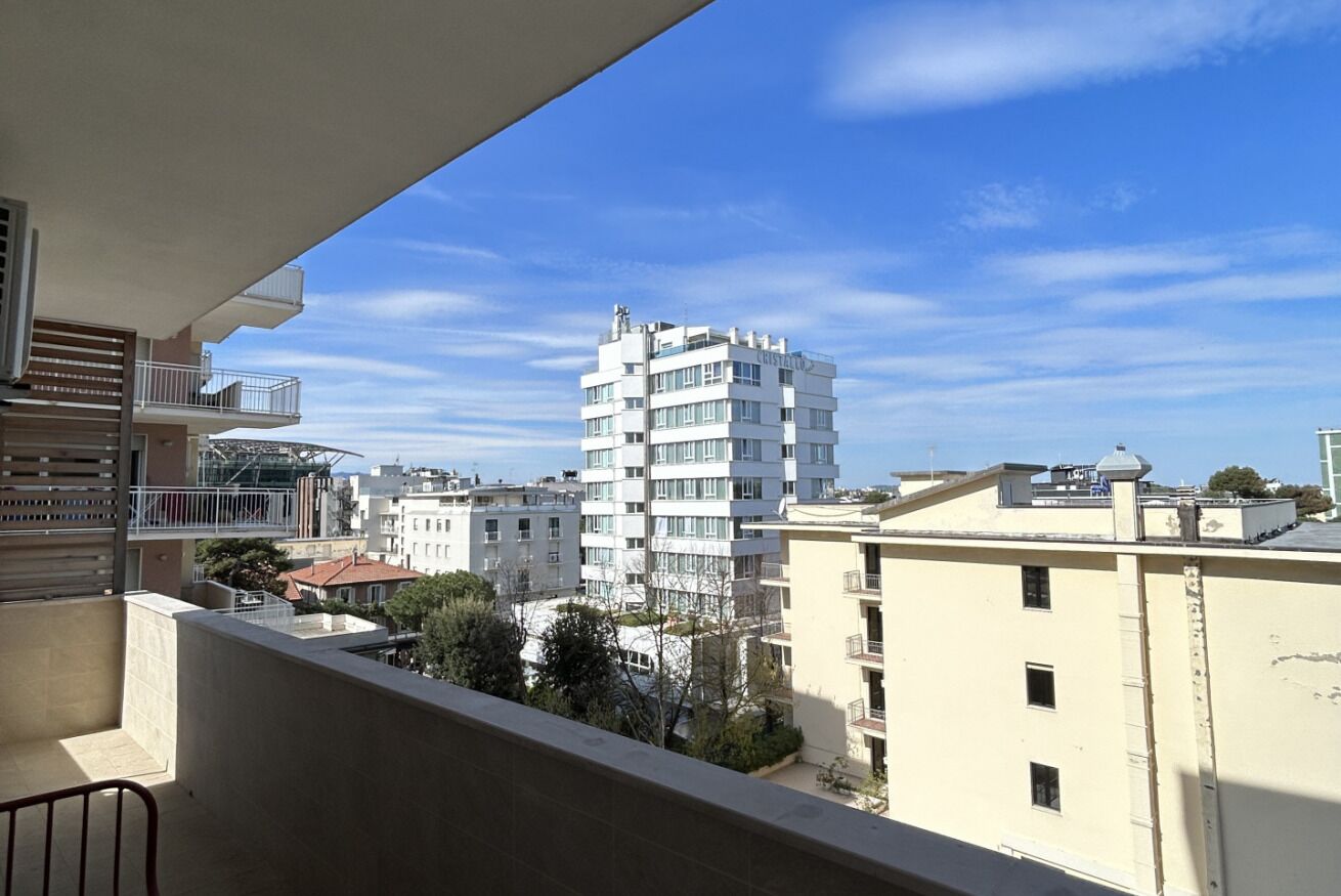 A balcony with a view of a multi-story building, other residential buildings, and trees.