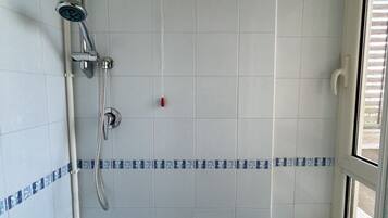 Een badkamer met witte betegelde wanden, een douche met handdouche en een raam met blinds.