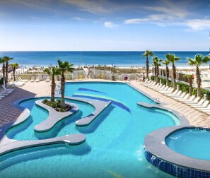 A swimming pool with a wavy design, surrounded by palm trees and lounge chairs, with a beach and ocean in the background. - Crystal Tower 1608 – Beachfront Pool-Lazy River-Gulf Views- Snowbird Wanted (Gulf Shores)