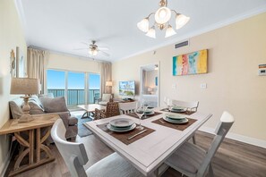 A dining area with a table set for four, a ceiling fan, and a large window with curtains. - Crystal Tower 1608 – Beachfront Pool-Lazy River-Gulf Views- Snowbird Wanted (Gulf Shores)