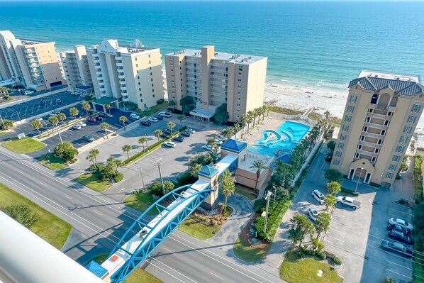 An aerial view of a beachfront hotel with multiple buildings, a parking lot, and a blue swimming pool. - Crystal Tower 1608 – Beachfront Pool-Lazy River-Gulf Views- Snowbird Wanted (Gulf Shores)