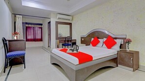 A hotel room with a bed, a desk, a chair, a nightstand, and an air conditioning unit. - Hotel New Simran Palace (Hyderabad)