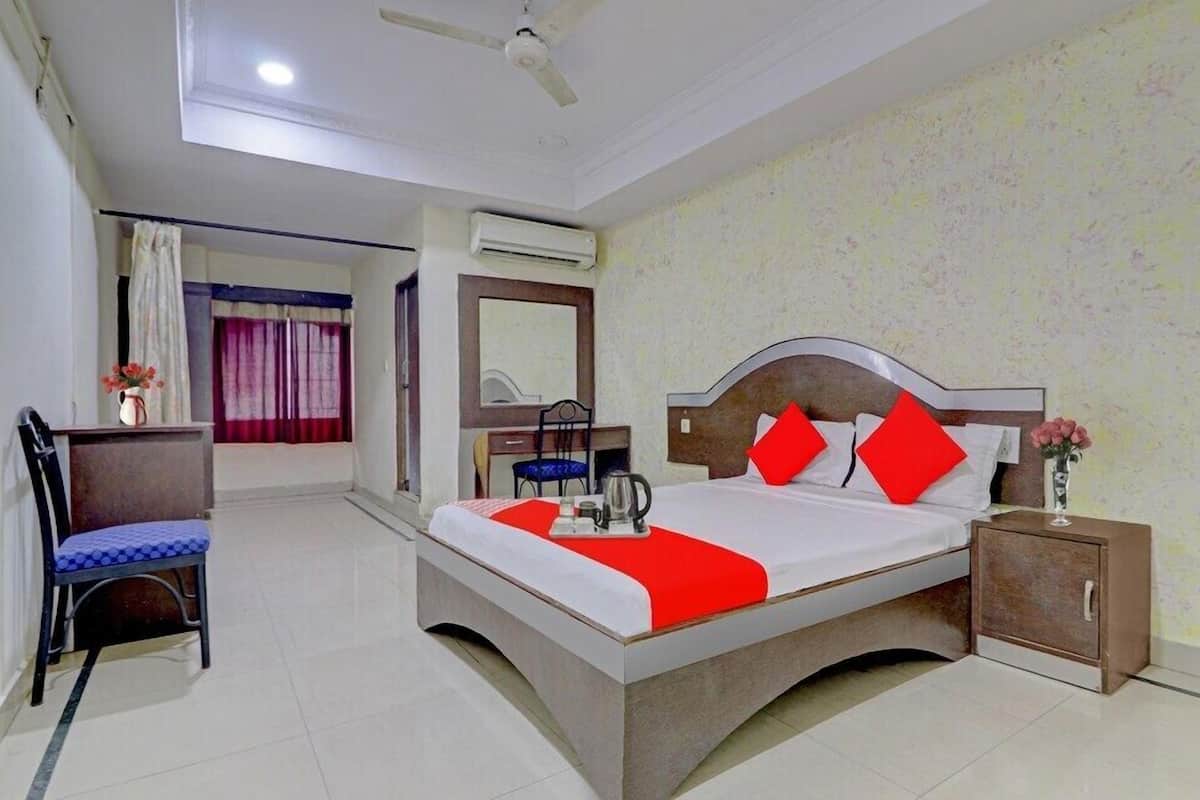 A hotel room with a bed, a desk, a chair, a nightstand, and an air conditioning unit.