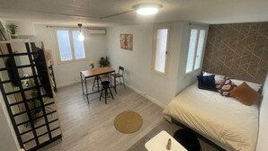 A compact room with a bed, a small table with chairs, a window, and a patterned wall. - Bagnol Cosy - Cosy apartment for 3 people, 30 min from Avignon (Bagnols-sur-Cèze)