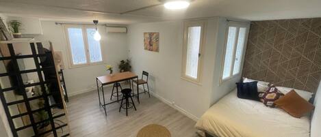 Une pièce de taille modeste, comprenant un lit, une petite table avec des chaises, une fenêtre et un mur décoré de motifs.