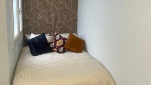 A small, single-bed room with a geometric-patterned headboard, a window on one side, and a plain white wall on the other. - Bagnol Cosy - Cosy apartment for 3 people, 30 min from Avignon (Bagnols-sur-Cèze)