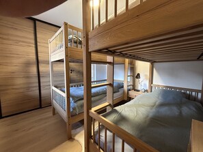 Une chambre avec un lit superposé, un plancher en bois, une table de chevet avec une lampe et une fenêtre.