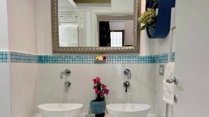 A bathroom with two white sinks, a mirror, and a blue vase with flowers. - Midorigami Jacuzzi zen suite Spanish Steps apt. (Roma)
