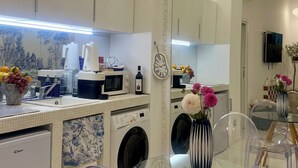 A modern kitchen with a microwave, sink, and washing machine. There is a dining area with a glass table and chairs. - Midorigami Jacuzzi zen suite Spanish Steps apt. (Roma)