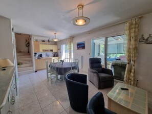 A spacious living area with a dining table, a sofa, and a chair. There is a kitchen area with cabinets and a window. - Holiday home for 8, near beach and sailing in Sarzeau, pets allowed (Sarzeau)