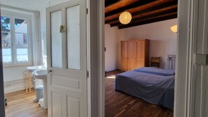 Una habitación con suelo de madera, una cama con cubrecama azul, un armario de madera y una puerta blanca con paneles de vidrio esmerilado.