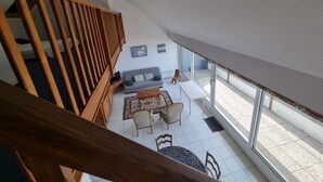 A spacious living area with a high ceiling, a wooden staircase, a sofa, a coffee table, and a view through large windows. - Duplex for 6, direct beach access in Arzon (Arzon)