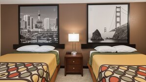 Une chambre d’hôtel avec deux lits, une table de chevet avec une lampe et deux tableaux représentant des paysages urbains accrochés aux murs.