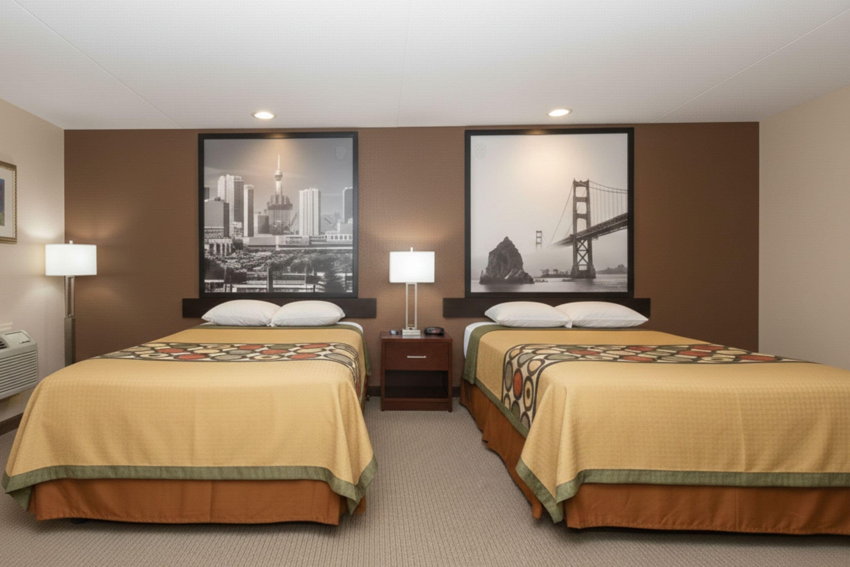 Une chambre d’hôtel avec deux lits, une table de chevet, une lampe et deux grandes images encadrées au mur.