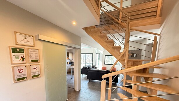 Un intérieur moderne avec un escalier en bois, un espace de vie doté d’un canapé et des certificats encadrés accrochés au mur.