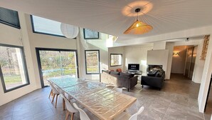 Un vaste espace de vie comprenant une grande table à manger, des meubles modernes et de grandes fenêtres offrant une vue sur l’extérieur.