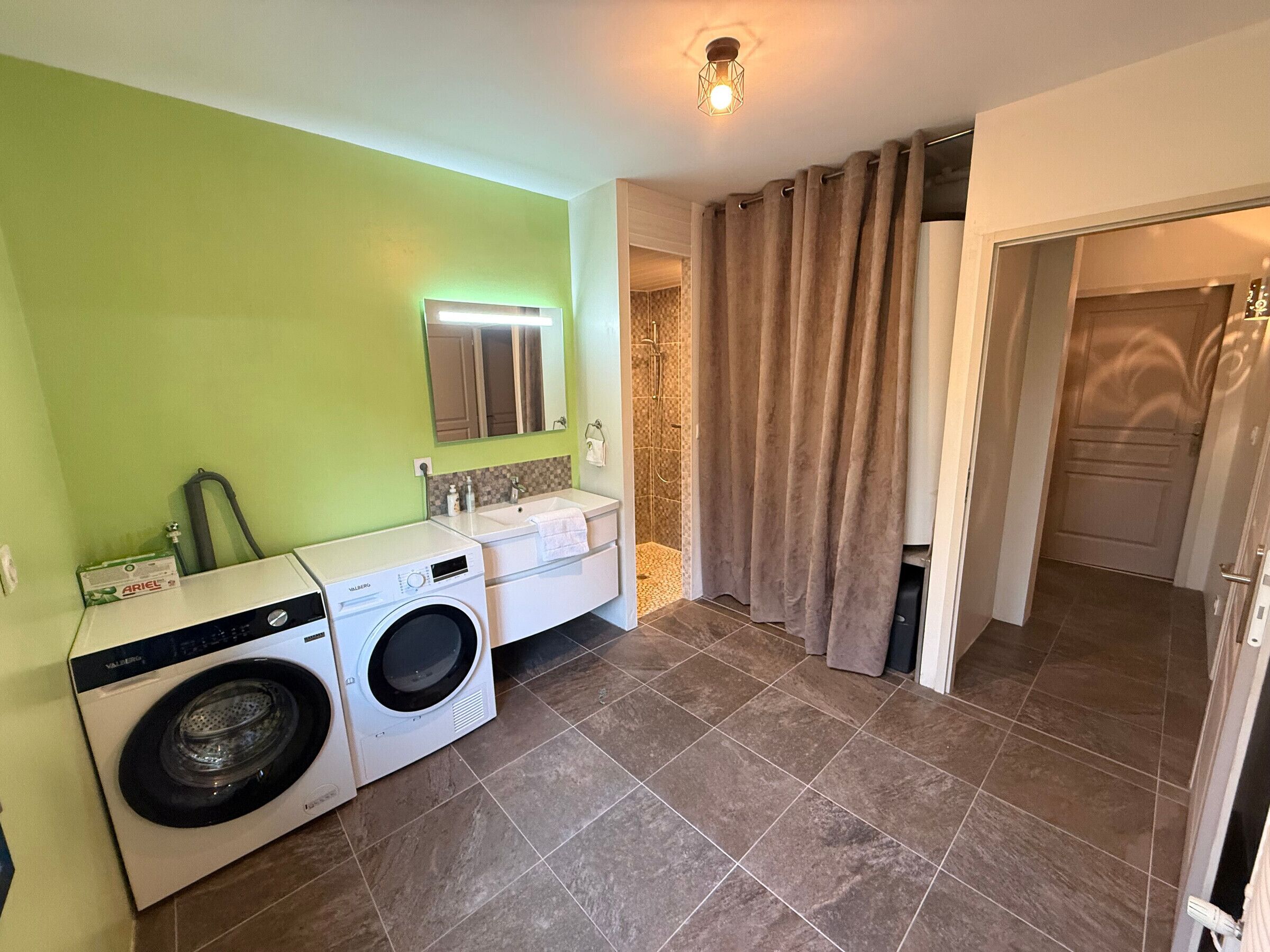 Een kleine badkamer met een wasmachine, wastafel en douchehoek.