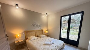 Une chambre dotée d’un grand lit, de deux lampes de chevet, d’une tête de lit en bois, d’une petite décoration en forme de branche et d’une porte-fenêtre coulissante donnant sur un espace extérieur.
