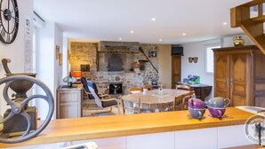 Una cocina con pared de piedra, armarios de madera, una mesa redonda y un reloj en la pared.