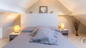 Un dormitorio con techo inclinado, una cama con manta texturizada, lámparas de noche, un adorno con forma de corazón y un jarrón con plantas secas.
