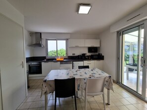A kitchen with a dining table, chairs, a window, and a view of greenery outside. - Renovated house near Kerfontaine Beach, 6 pers., pets allowed, 3 bedrooms (Sarzeau)