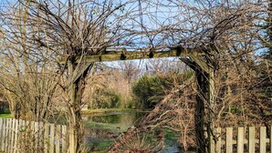 A wooden pergola arching over a pathway leading to a pond, surrounded by trees and a wooden fence. - Charming accommodation with park and pond in Mers-sur-Indre (Mers-sur-Indre)