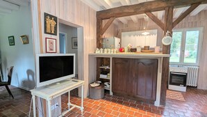 A rustic kitchen with exposed wooden beams, a brick floor, and a television on a white stand. - Charming accommodation with park and pond in Mers-sur-Indre (Mers-sur-Indre)