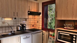 Eine kleine Küche mit Holzausstattung, einer eingebauten Mikrowelle, einer Kaffeemaschine und einem Fenster mit Blick auf Bäume.